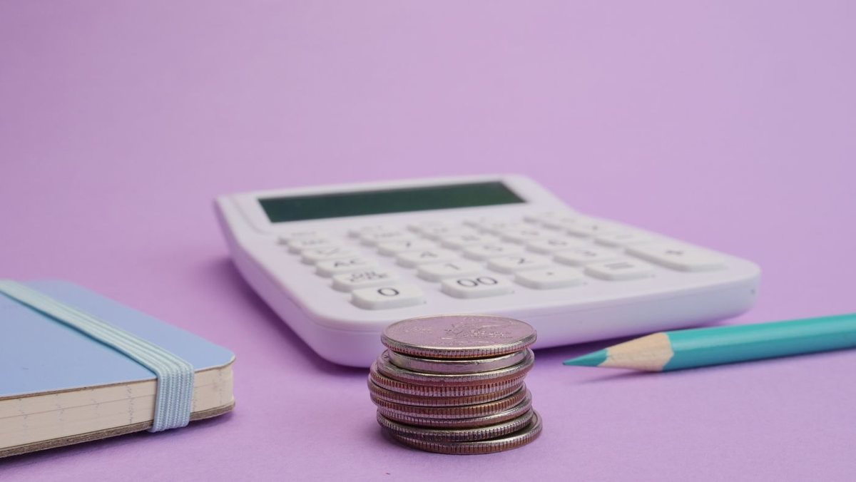 Calculator and stacked coins beside a notebook