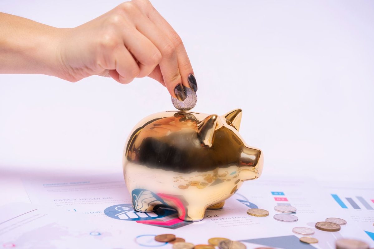 A hand placing a coin into a gold piggy bank