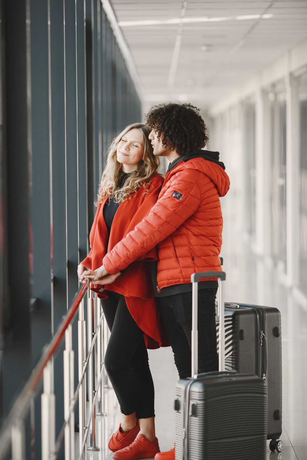 Two travellers with wheeled luggage waiting by an airport window